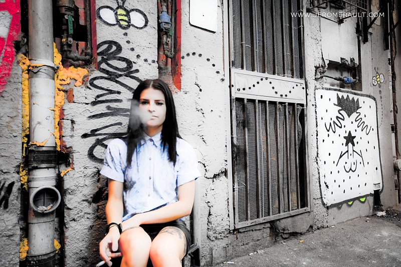 Tattooed girl smoking in alleyway.